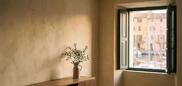Intérieur d'appartement provençal repeint en badigeon de chaux ocre, fenêtre à volets verts ouverte sur le vieux port de Saint-Tropez