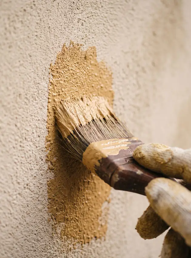 Application au pinceau d'un badigeon de chaux ocre sur un mur enduit, technique employée en façade à Saint-Tropez
